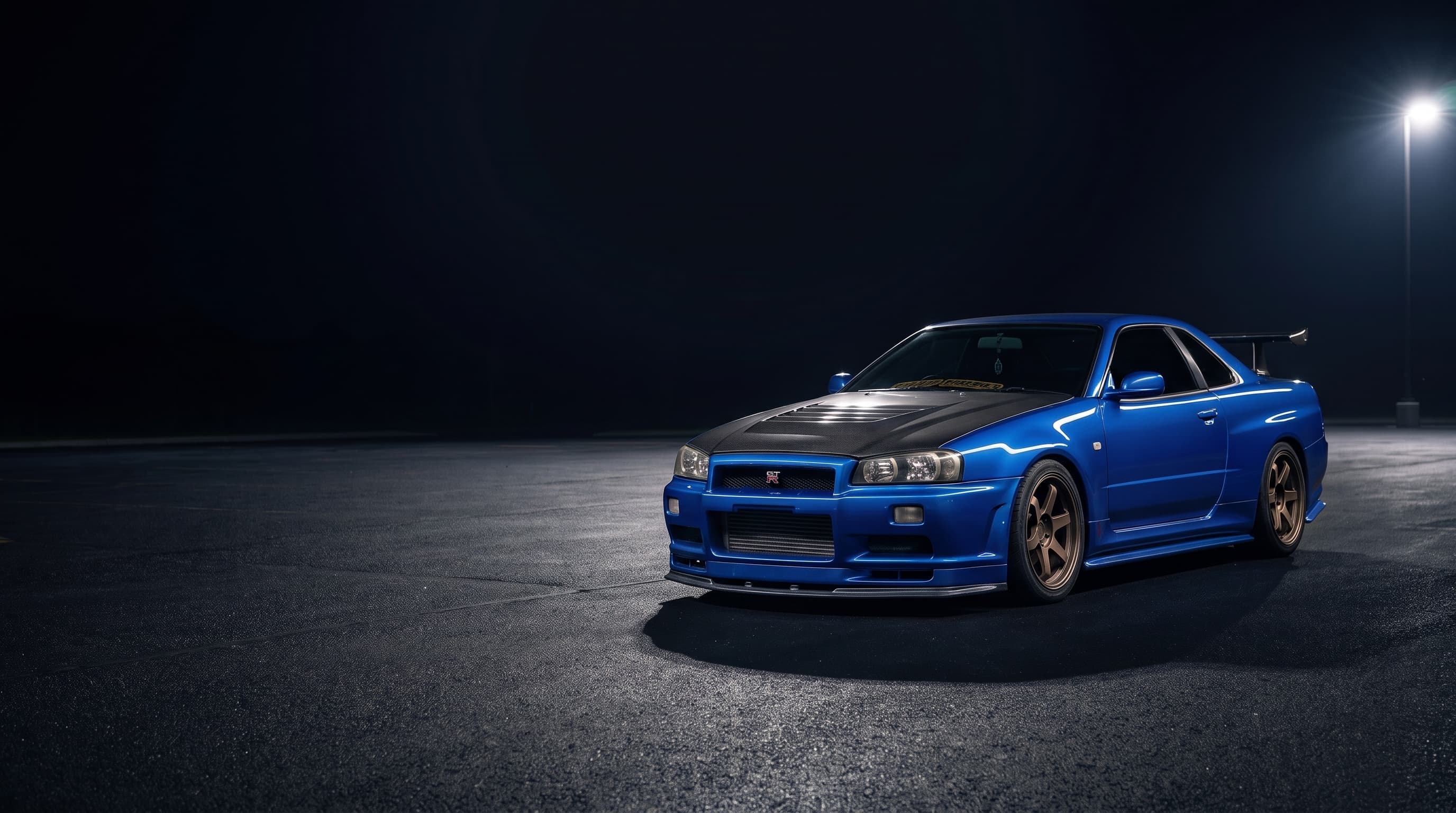 A Nissan Skyline R34 GT-R V-Spec II, the owner's own car, lit by a single overhead lamp on an empty lot at night.